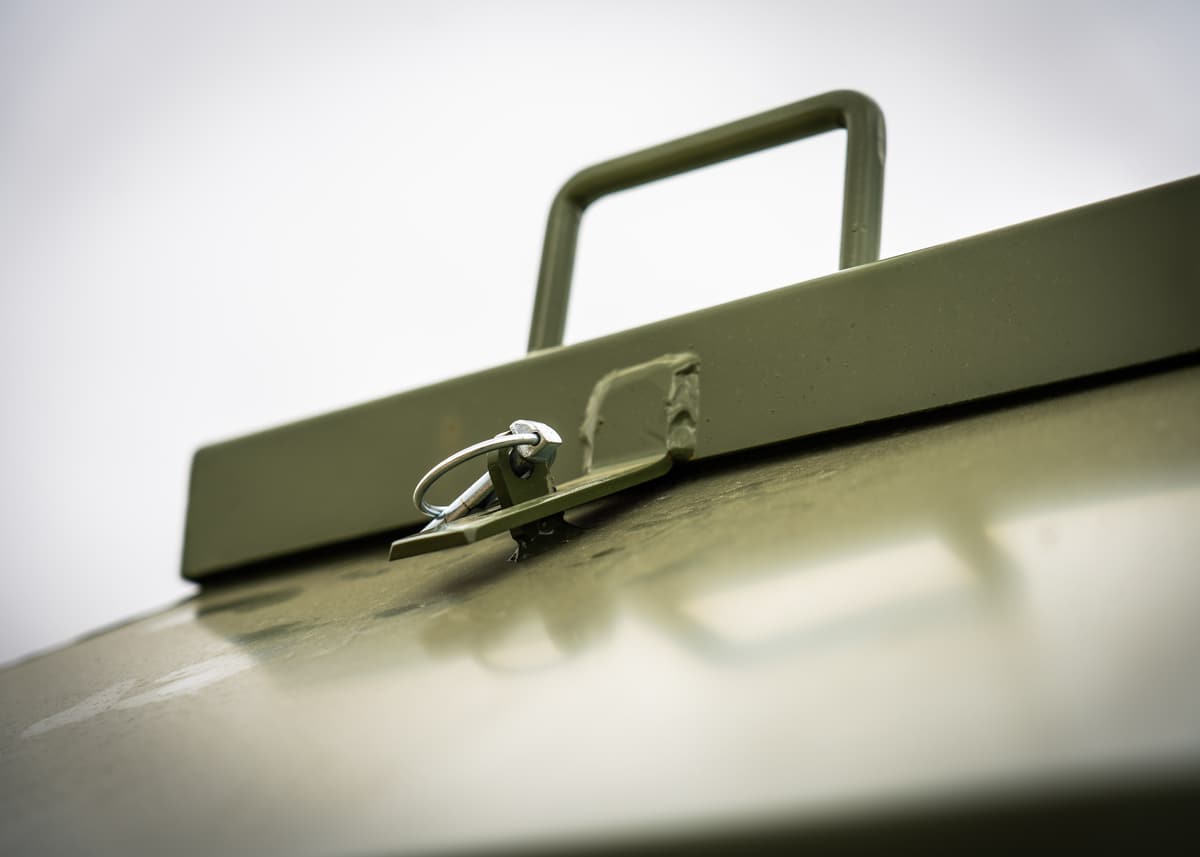 Close-up of the feeder lid: a bent-steel handle and a pinned latch, both powder-coated olive.